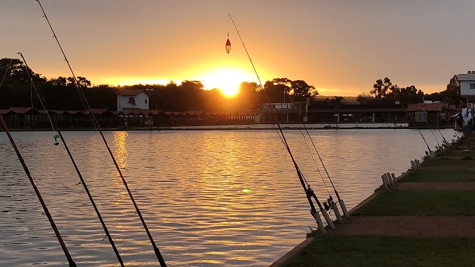 Pôr do sol sobre o lago do Clube Pescar com varas de pesca em primeiro plano